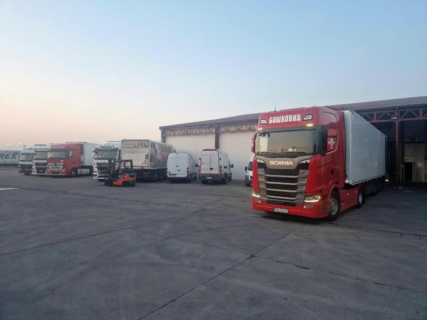 Crvena Scania S sa hladnjačom ispred skladišta u zoru